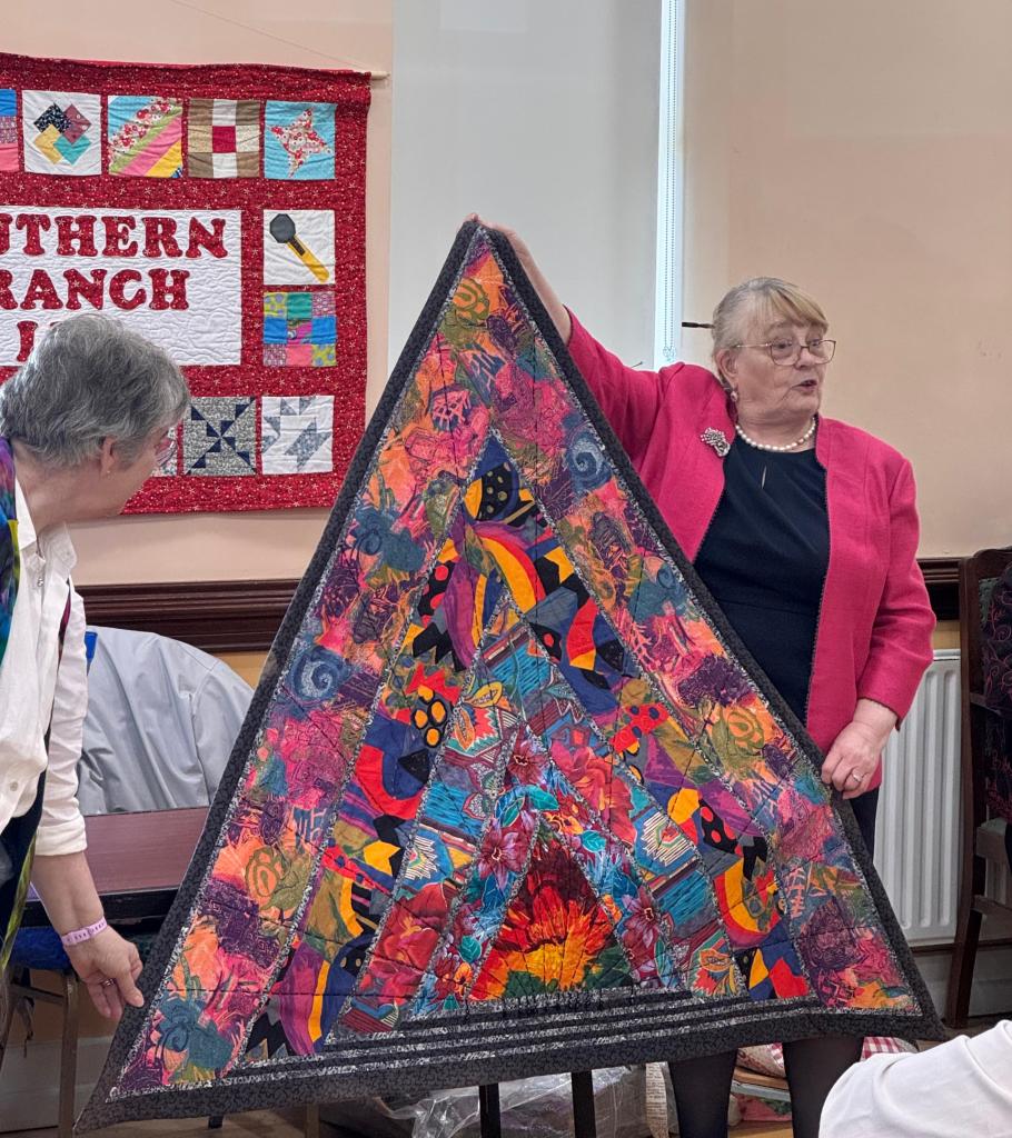 Loretta O'Brien holds a large triangle quilt in shades of red and purple.