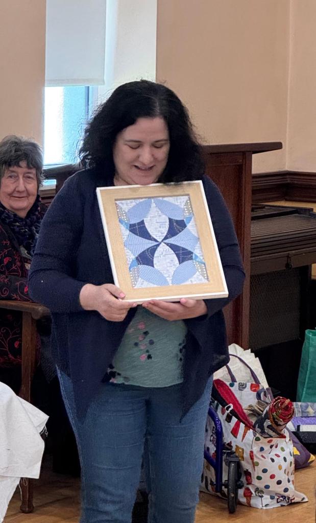 Ruth Bourke holds a framed challenge made of blue fabrics, with symmetrical shapes.